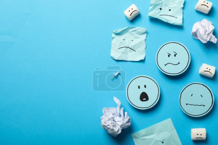 Papers and marshmallows with sad emoji on blue background, space for text
