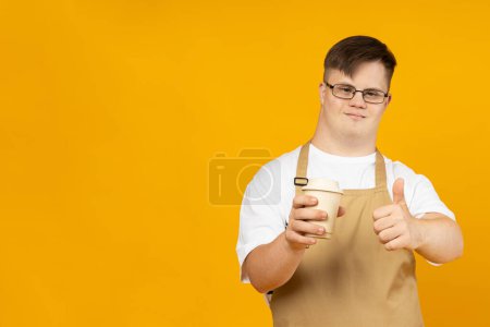 A smiling young man with cerebral palsy in glasses as a barista in an apron and with coffee. World Genetic Diseases Day concept, place for text