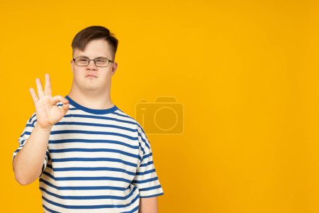 Photo for Smiling young man with cerebral palsy in glasses in a striped t-shirt on a yellow background. World Genetic Diseases Day concept, place for text - Royalty Free Image