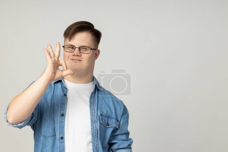 Photo for A smiling young man with cerebral palsy in glasses, jeans and a white T-shirt poses for the camera. World Genetic Diseases Day concept, place for text - Royalty Free Image