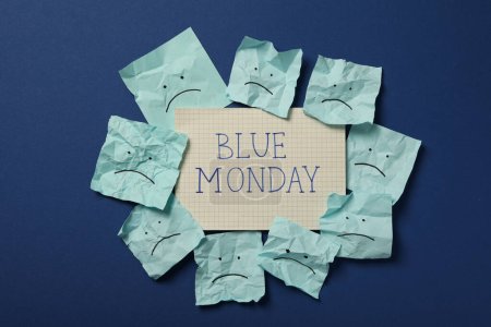 Paper with text Blue Monday and notes with sad emoji on blue background, top view
