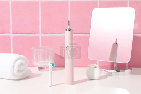 Téléchargez les photos : Brosse à dents électrique, serviette et miroir sur table sur fond rose - en image libre de droit