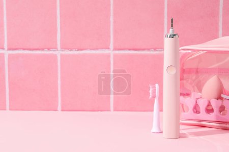 Téléchargez les photos : Brosse à dents électrique et sac cosmétique sur fond rose, espace pour le texte - en image libre de droit