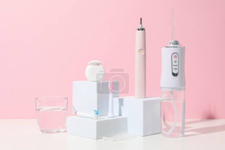 Téléchargez les photos : Brosse à dents électrique, irrigateur et verre d'eau sur fond rose - en image libre de droit