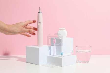 Téléchargez les photos : Brosse à dents électrique sur blocs, verre d'eau et main féminine sur fond rose - en image libre de droit