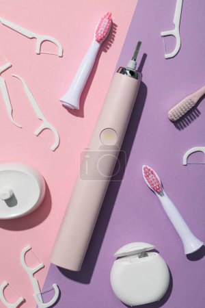 Téléchargez les photos : Brosse à dents électrique et fil dentaire sur fond rose et violet, vue de dessus - en image libre de droit