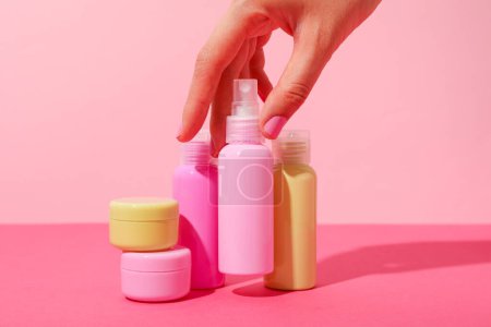 Photo for Cosmetic bottles and female hands on pink background - Royalty Free Image
