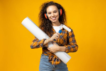Photo for An attractive, young girl in construction headphones and with a roller and paper in her hands - Royalty Free Image