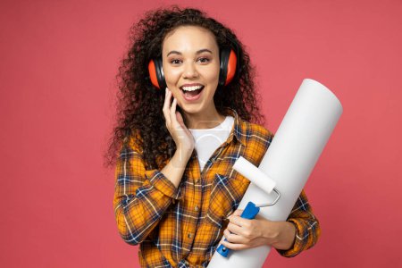 Photo for An attractive, young girl in construction headphones and with a roller and paper in her hands - Royalty Free Image
