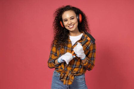Photo for An attractive, young girl in construction headphones and with a hammer in her hands - Royalty Free Image