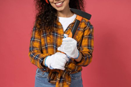 Photo for An attractive, young girl in construction headphones and with a hammer in her hands - Royalty Free Image