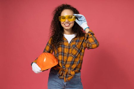 Photo for An attractive, young girl in construction glasses and with a hard hat in her hands - Royalty Free Image