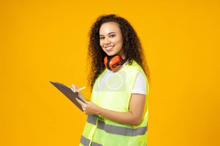 Photo for Attractive young girl in noise-reducing headphones and a folder against a yellow background - Royalty Free Image