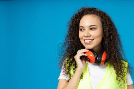 Photo for Attractive, young girl in noise-reducing headphones against a blue background - Royalty Free Image