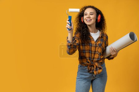 Photo for A girl in construction headphones and with a roller and paper in her hands - Royalty Free Image