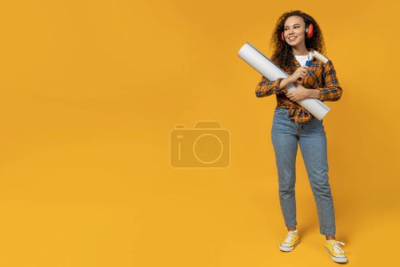 Photo for A girl in construction headphones and with a roller and paper in her hands - Royalty Free Image