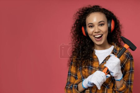 Photo for A girl in construction headphones and with a hammer in her hands - Royalty Free Image