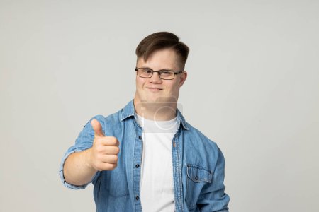 Foto de Un joven sonriente con parálisis cerebral en gafas, jeans y una camiseta blanca posa para la cámara. Concepto del Día Mundial de las Enfermedades Genéticas - Imagen libre de derechos
