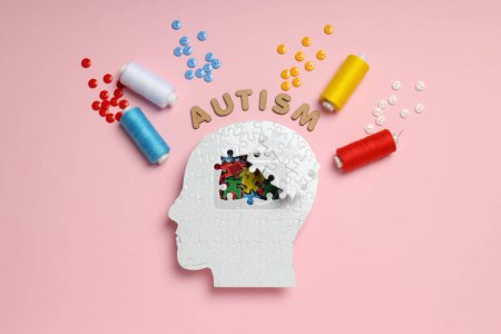 Puzzle head, word autism, threads and buttons on pink background, top view