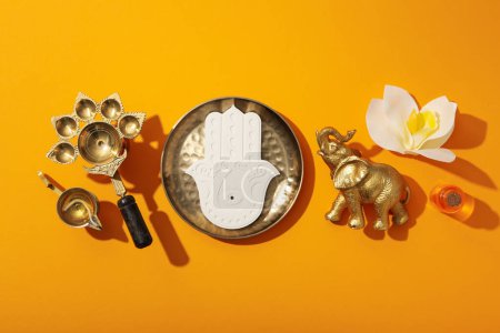 Photo for Copper utensils, elephant figurine, Hamsa and flower on orange background, top view - Royalty Free Image