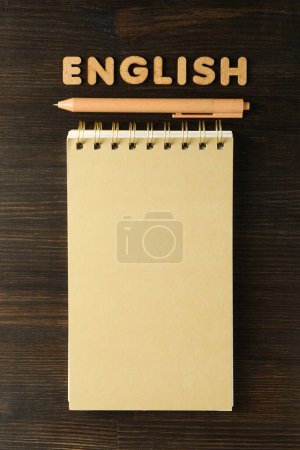 Foto de La palabra "inglés" y un cuaderno, el concepto de aprender inglés, sobre un fondo oscuro. - Imagen libre de derechos
