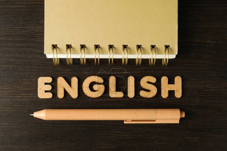 Foto de La palabra "inglés" y un cuaderno, el concepto de aprender inglés, sobre un fondo oscuro. - Imagen libre de derechos