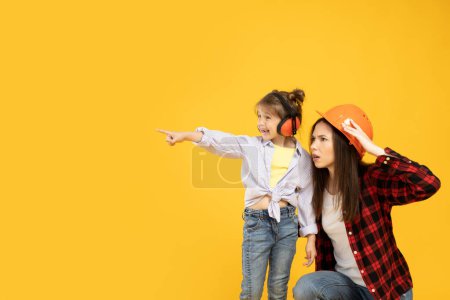 Téléchargez les photos : Mère et fille en accessoires pour la construction, sur fond jaune. - en image libre de droit