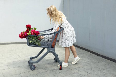 Une belle fille avec un chariot avec des fleurs dans la rue.
