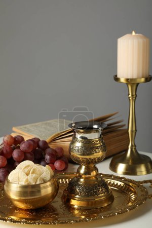 Foto de Vela, libro, uvas, pan litúrgico, cruz dorada y copa sobre la mesa sobre fondo gris - Imagen libre de derechos