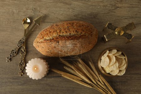 Bread, spikelets and candle on wooden background, top view