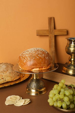 Foto de Cruz de madera y copa sobre libro, pan y uvas sobre fondo naranja - Imagen libre de derechos