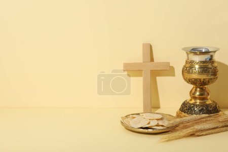 Wooden cross, liturgical bread, spikelets and cup on light background, space for text