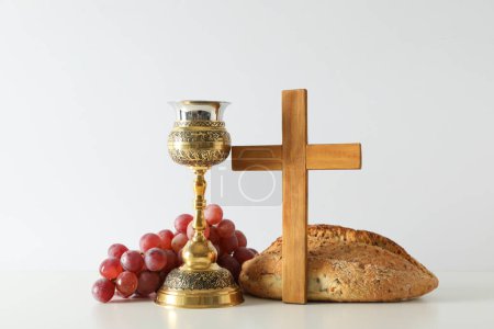 Bread, cup, grapes and wooden cross on white background