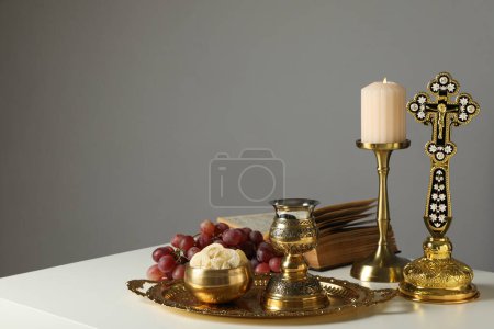 Candle, book, grapes, liturgical bread, golden cross and cup on table on gray background, space for text