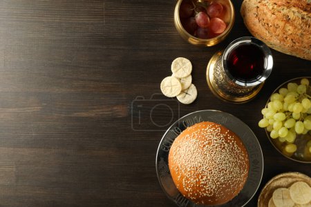 Bread, grapes in bowls and cup of wine on wooden background, space for text