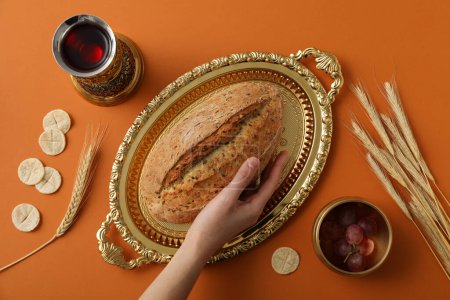 Foto de Pan en bandeja dorada, mano, espiguillas, uvas y copa de vino sobre fondo naranja, vista superior - Imagen libre de derechos