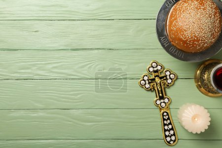 Bread, cross, cup of wine and candle on green wooden background, space for text