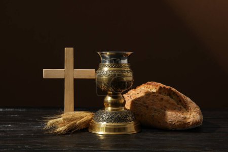 Wooden cross, bread, spikelets and cup on brown background