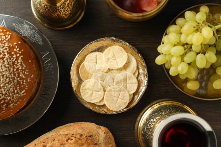 Bread, grapes in bowls and cup of wine on wooden background, top view