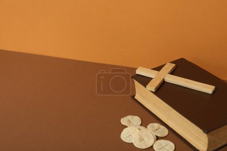 Foto de Cruz de madera sobre libro y pan litúrgico sobre fondo marrón, espacio para texto - Imagen libre de derechos