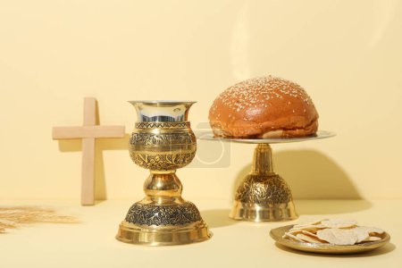 Wooden cross, bread and cup on light background