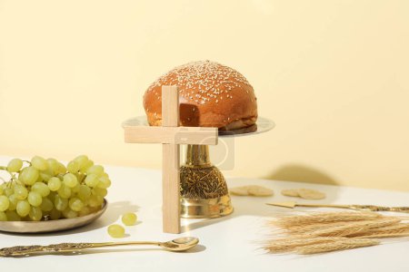 Foto de Cruz de madera, pan, uvas y espiguillas en la mesa sobre fondo beige - Imagen libre de derechos