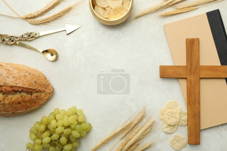 Bread, grapes, wooden cross on book and spikelets on light background, space for text