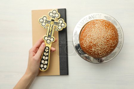 Bread, spikelets, book and cross in hand on white background, top view