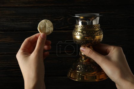 Foto de Pan litúrgico y copa de oro en las manos sobre fondo de madera, de cerca - Imagen libre de derechos