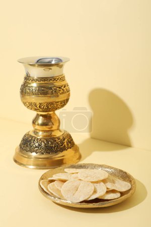 Liturgical bread and cup on light yellow background