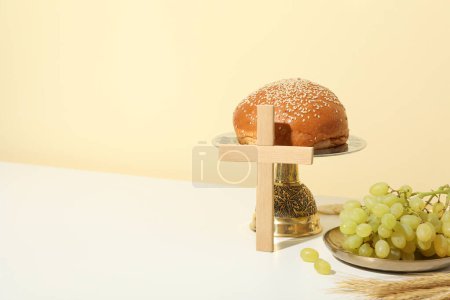 Foto de Cruz de madera, pan, uvas y espiguillas en la mesa sobre fondo beige, espacio para texto - Imagen libre de derechos