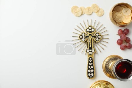 Bread, cup of wine, grapes and cross on white background, space for text