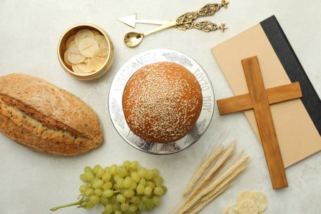 Bread, grapes, wooden cross on book and spikelets on light background, top view