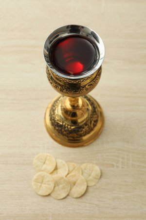 Cup of wine and liturgical bread on a wooden background, close up